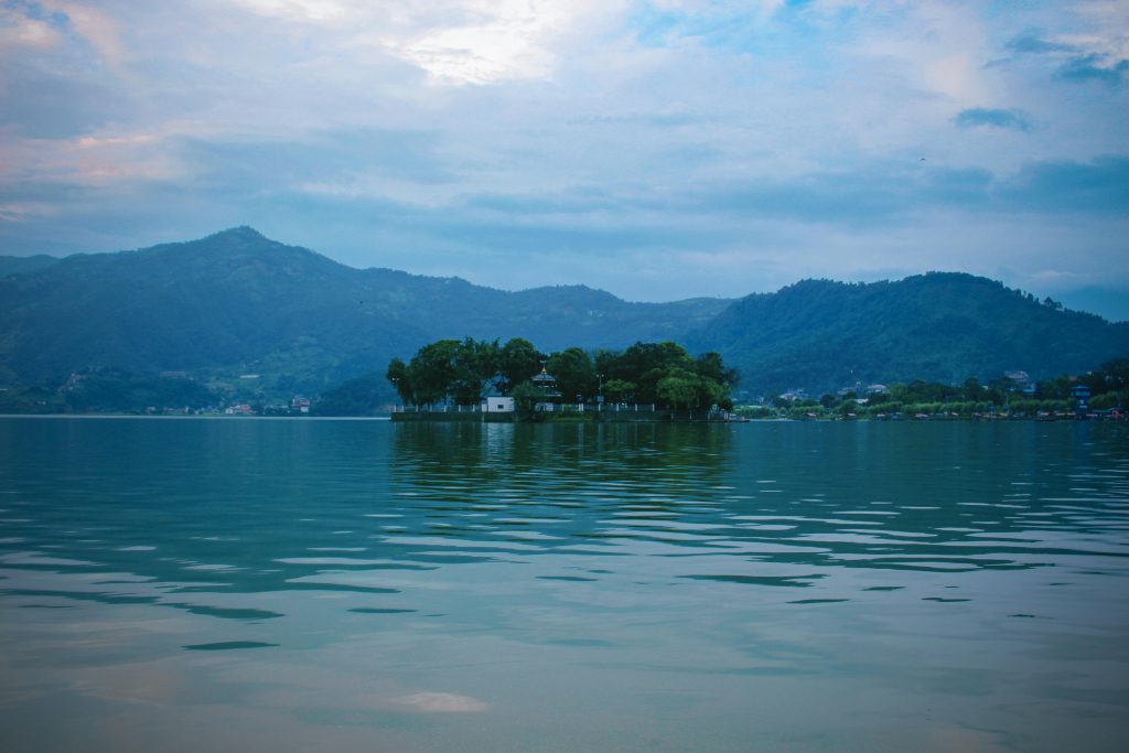 Serene view of Fewa Lake with surrounding mountains in Pokhara, Nepal, under a cloudy sky.